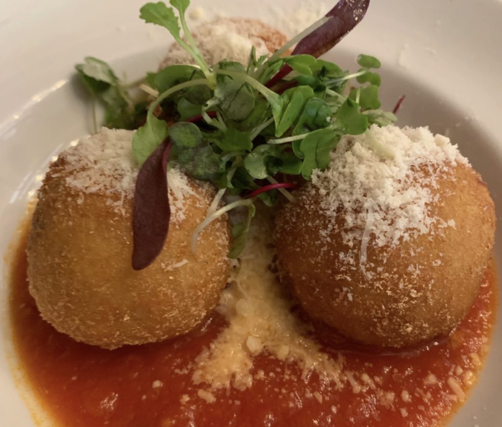 3 arancini balls with micro greens sitting on red sauce