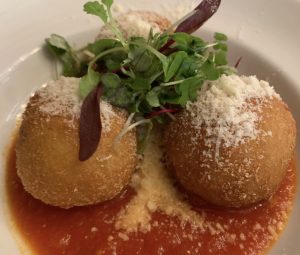 3 arancini balls with micro greens sitting on red sauce