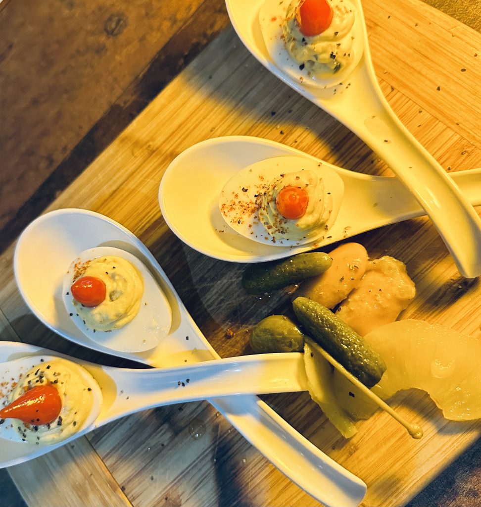 four deviled eggs topped with red peppers on individual serving spoons at Bites & Bubbles Orlando